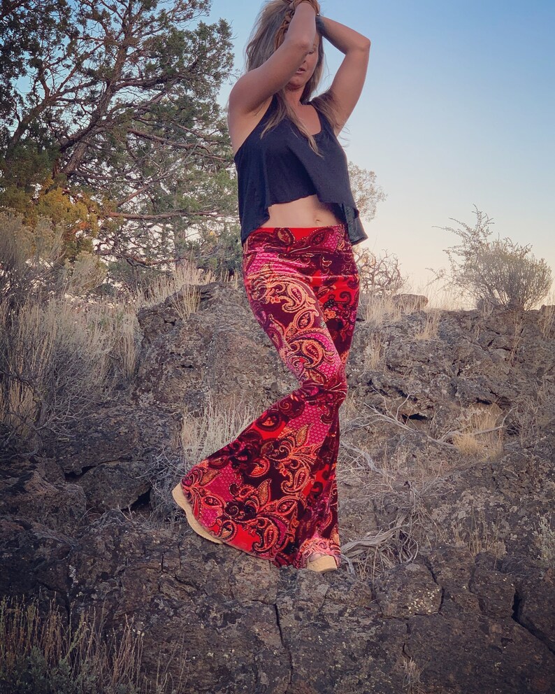 Puede incluir: Una mujer con un top negro sin mangas y pantalones acampanados de terciopelo con estampado paisley rojo y rosa. Los pantalones tienen una pierna ancha.