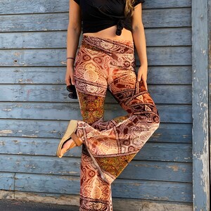 May include: A pair of wide-leg pants with a paisley print in shades of brown, orange, and green. The pants are made of a soft, velvety fabric and have a wide, flowing leg.