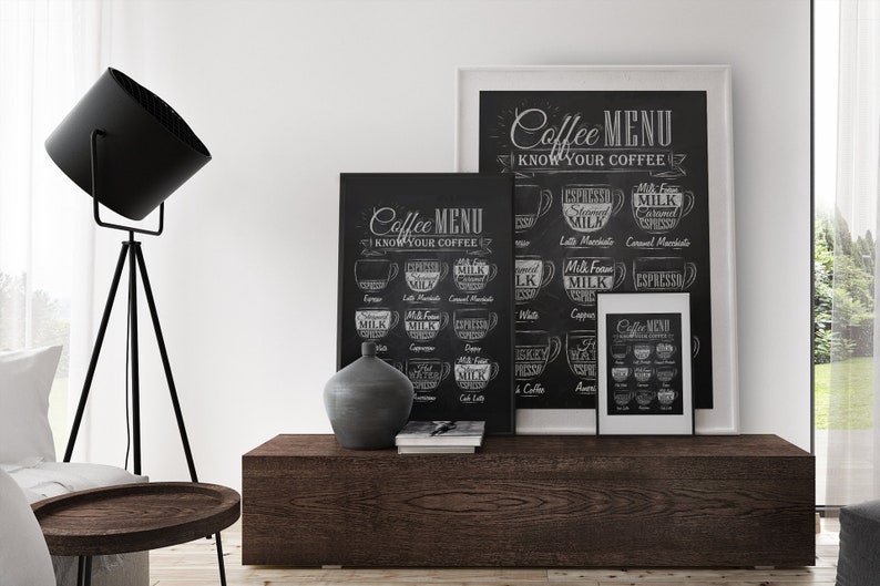 K&ouml;nnte beinhalten: Zwei schwarze gerahmte Tafeln mit wei&szlig;em Text und Illustrationen von Kaffeetassen. Die Schilder zeigen "Coffee Menu Know Your Coffee". Die Schilder h&auml;ngen an einer wei&szlig;en Wand &uuml;ber einem dunkelbraunen Holztisch.