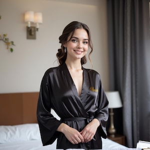 Woman wearing elegant black satin personalized robe with gold embroidered name. Perfect for bridesmaid robes, bridal party robes, and mother of the bride robes. Soft silk kimono dressing gown ideal for weddings, bridesmaid proposals, or luxury lounge wear.