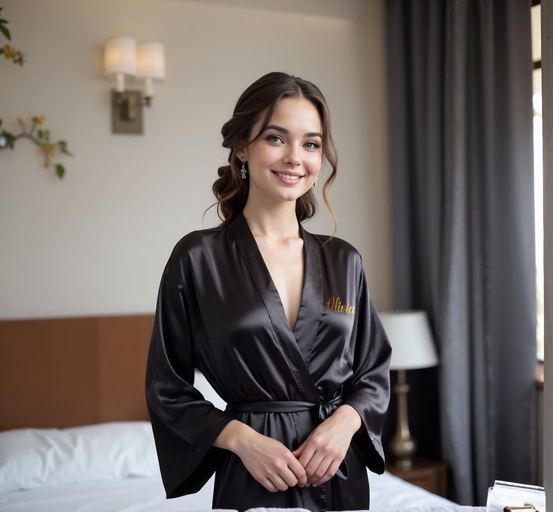 Woman wearing elegant black satin personalized robe with gold embroidered name. Perfect for bridesmaid robes, bridal party robes, and mother of the bride robes. Soft silk kimono dressing gown ideal for weddings, bridesmaid proposals, or luxury lounge wear.