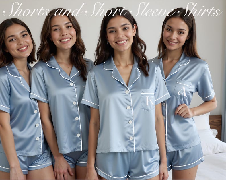 Four women smile while wearing matching light blue satin pajama sets featuring short-sleeve button-down shirts and matching shorts with white piping. Two pajamas are personalized with initials “K” and “A” on the front pocket. The soft, glossy satin fabric and relaxed fit make these personalized pajamas perfect for bridesmaid proposals, summer bridal party gifts, bachelorette weekends, or getting-ready photos. A beautiful choice for custom women’s loungewear with a lightweight and elegant finish.