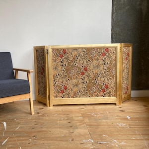 May include: A decorative folding screen with a gold frame and a floral design in brown, red, and green. A blue armchair with wooden arms is positioned to the left. The screen is a room divider, a decorative furniture item.