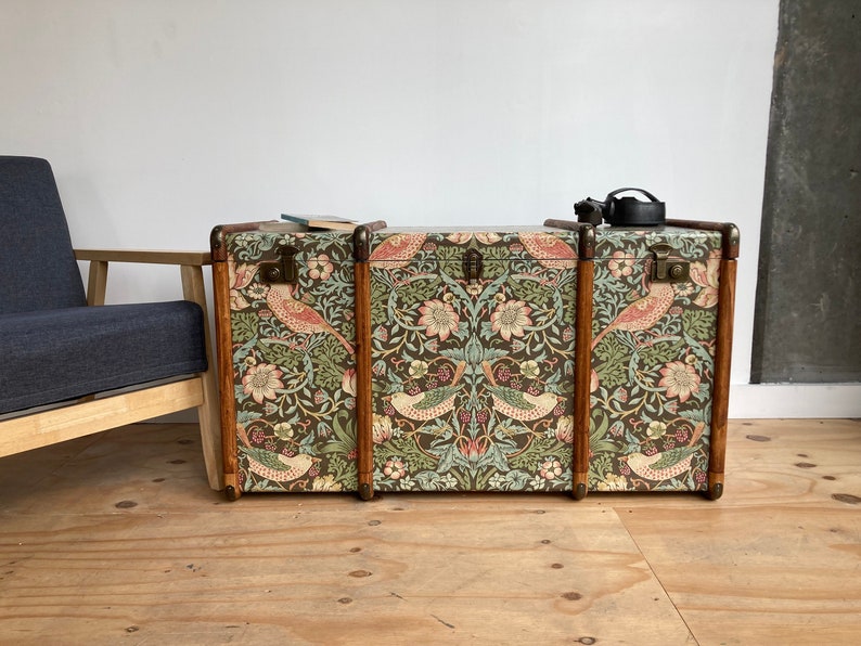 May include: Three vintage wooden storage trunks with floral patterned fabric covering. The fabric features a repeating pattern of birds, flowers, and leaves in shades of green, pink, and brown.