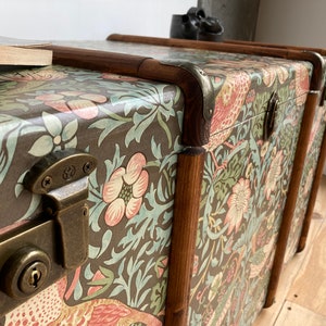 May include: Three vintage-style wooden storage trunks with a floral pattern and brass hardware. The trunks are stacked on top of each other.