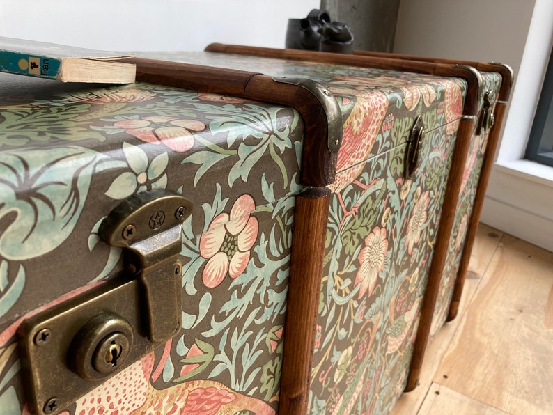 May include: Three vintage-style wooden storage trunks with a floral pattern and brass hardware. The trunks are stacked on top of each other.