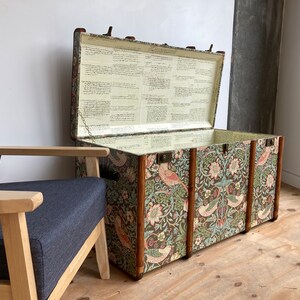 May include: A vintage floral patterned storage trunk with a wooden frame and brass hardware. The trunk is open and the inside is lined with white paper.
