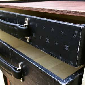 May include: A black wooden box with two drawers. The drawers have black leather handles and a black and white patterned design. The box is open and the drawers are pulled out.