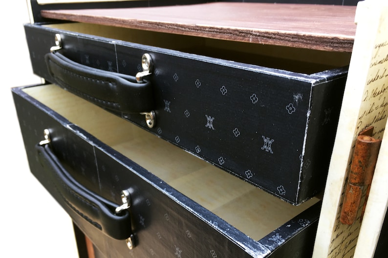 May include: A black wooden box with two drawers. The drawers have black leather handles and a black and white patterned design. The box is open and the drawers are pulled out.