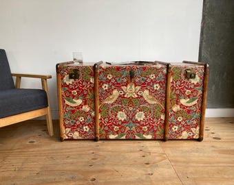May include: A vintage wooden trunk with a red, green, and white floral pattern. The trunk has brass hardware and is decorated with a floral design.