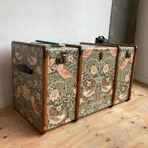 May include: Three vintage wooden storage trunks with a floral and bird patterned fabric covering. The trunks are stacked on top of each other.