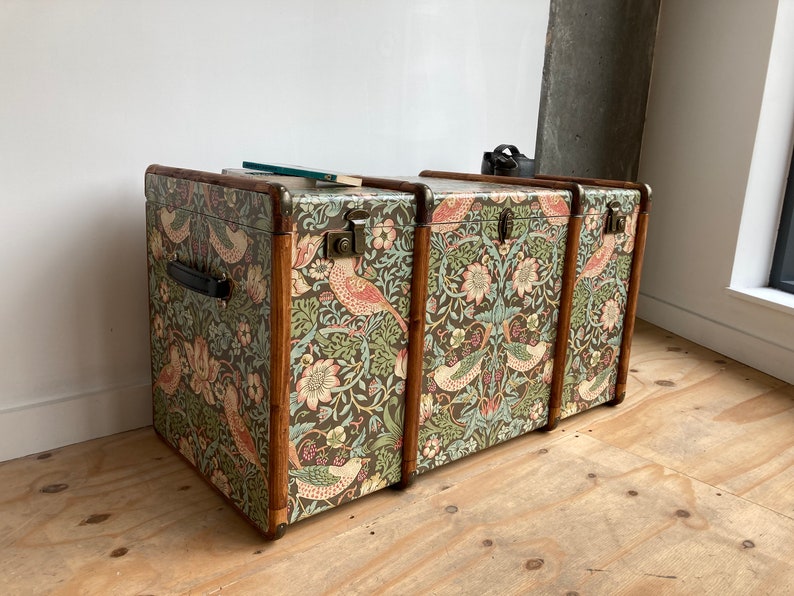 May include: Three vintage wooden storage trunks with a floral and bird patterned fabric covering. The trunks are stacked on top of each other.