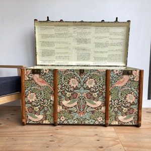 May include: A vintage-style storage trunk with a floral and bird patterned design. The trunk is open and the inside is lined with white paper. The trunk is made of wood and has brass hardware.