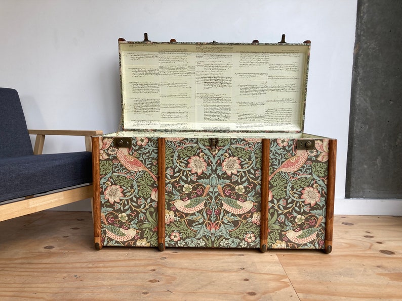 May include: A vintage-style storage trunk with a floral and bird patterned design. The trunk is open and the inside is lined with white paper. The trunk is made of wood and has brass hardware.