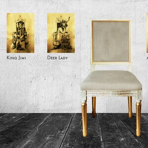 May include: Four framed black and white illustrations of people in costumes, with the titles "Queen", "King Jimi", "Deer Lady", and "Astronaut" below each image. A white chair with a beige cushion and gold legs sits in front of the wall.