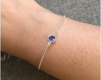 May include: A delicate silver chain bracelet with a single blue gemstone.