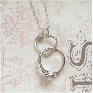 May include: Silver necklace with a heart pendant and a ring with a clear stone. The ring is threaded through the heart pendant.
