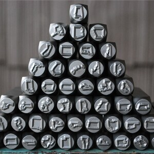 May include: A collection of metal letter stamps arranged in a pyramid shape. The stamps are silver in color and have various letter and symbol designs.