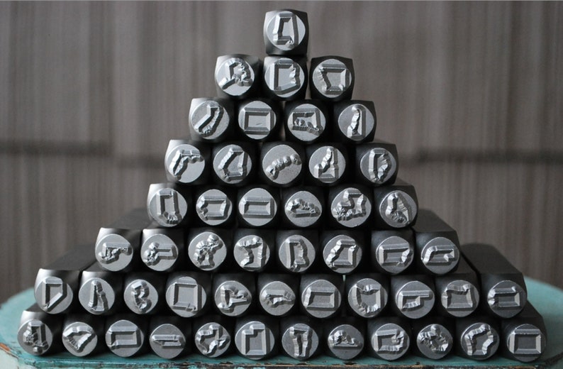 May include: A collection of metal letter stamps arranged in a pyramid shape. The stamps are silver in color and have various letter and symbol designs.