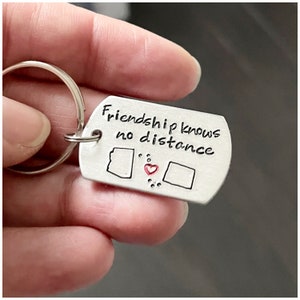 May include: Silver keychain with the text "Friendship knows no distance" and two outlined states connected by a red heart.