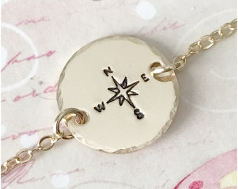 May include: Gold chain bracelet with a round pendant featuring a compass design with a star in the center and the letters N, S, E, and W around the star.