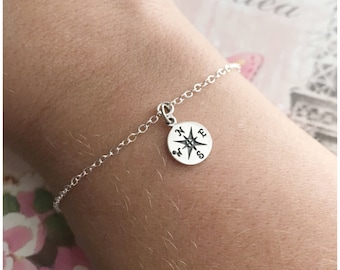 May include: A silver chain bracelet with a compass charm. The compass charm has the directions N, E, S, and W engraved on it.