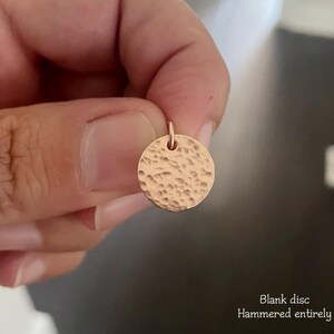 May include: A small, circular rose gold pendant featuring a textured, hammered finish across its entire surface. The disc includes a small jump ring at the top for attachment. The text "Blank disc Hammered entirely" is printed in the corner.