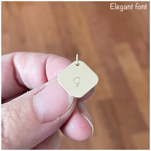 May include: Gold square charm with the letter "G" engraved in an elegant font.