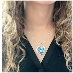 May include: A silver necklace with a round pendant featuring a snowflake design. The pendant has a blue background and the snowflake is cut out of the metal.