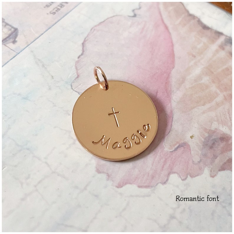 May include: A gold-toned round pendant with the name "Maggie" engraved in a cursive font and a small cross above the name.