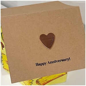 Puede incluir: Una tarjeta marr&oacute;n con el texto "Happy Anniversary!" impreso en ella. Un peque&ntilde;o amuleto de coraz&oacute;n dorado con la fecha "9-24-2017" grabada en &eacute;l est&aacute; unido a la tarjeta.