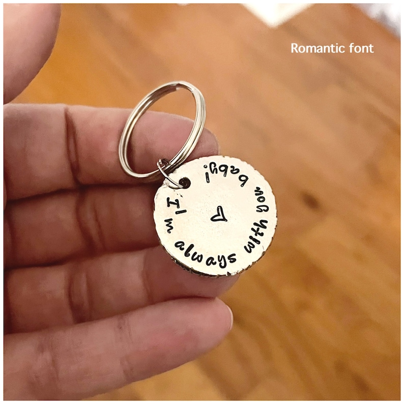K&ouml;nnte beinhalten: Silberner Schl&uuml;sselanh&auml;nger mit einem runden Anh&auml;nger, auf dem in romantischer Schrift "Ich bin immer bei dir" steht, mit einem kleinen Herzsymbol.