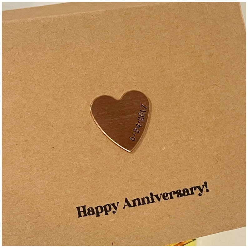 Puede incluir: Una tarjeta marr&oacute;n con el texto "Happy Anniversary!" y un peque&ntilde;o amuleto de cobre en forma de coraz&oacute;n con la fecha "6-24-2017" grabada en &eacute;l.