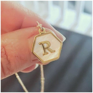 May include: Gold necklace with a hexagonal pendant featuring a white mother-of-pearl inlay and the letter "R" in gold.