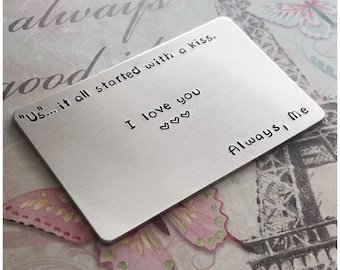 Op de afbeelding: Een zilveren metalen sleutelhanger met de tekst "Us... it all started with a kiss. I love you ♡♡♡ Always, Me" erop gegraveerd.