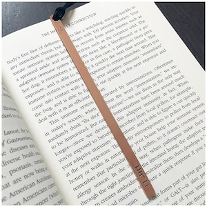 May include: A brown leather bookmark with the text "THE IMMUNITY CONNECTION" printed on it. The bookmark is placed on a page of an open book with text about the immune system.