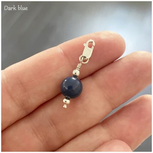 May include: A dark blue bead charm with a silver clasp. The bead is round and smooth.