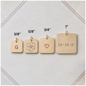 May include: Four square gold-toned metal charms with jump rings. The charms are labeled with sizes 3/8 inch, 5/8 inch, 3/4 inch, and 1 inch. The charms feature an engraved letter G, a flower illustration, a heart outline, and the date 05.08.21.