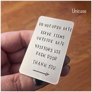 Puede incluir: Una placa rectangular de metal plateado con esquinas redondeadas que presenta el texto estampado: DO NOT OPEN GATE, LEAVE ITEMS OUTSIDE GATE, VISITORS USE BACK DOOR, THANK YOU, y una flecha hacia la derecha. La palabra Unicase aparece arriba a la derecha.