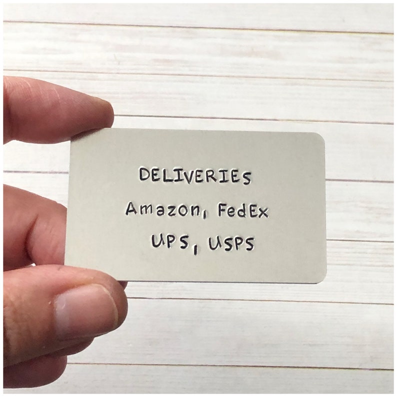 Puede incluir: Una placa rectangular de metal plateado con esquinas redondeadas que presenta texto negro estampado que dice DELIVERIES, Amazon, FedEx, UPS, USPS. La superficie met&aacute;lica tiene un acabado mate liso y las letras est&aacute;n claramente hendidas.