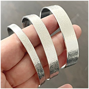 May include: Four silver metal bangles with a floral pattern etched into the surface.