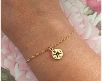 May include: A gold chain bracelet with a compass charm. The compass charm has a black star in the center and the letters N, E, S, and W around the edge.