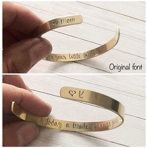 Puede incluir: Dos pulseras de metal dorado con texto grabado. La pulsera superior dice "Mom" y "Forever your little girl." La pulsera inferior dice "K" y "Today a bride, forever your".