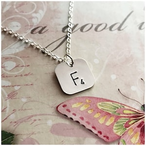 May include: Silver necklace with a square pendant that says "F4" on it. The pendant is hanging over a pink and green butterfly.