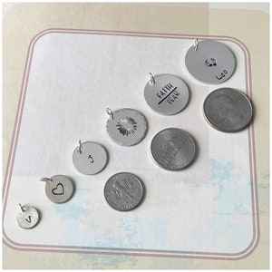 May include: A collection of silver charm pendants with various designs, including a heart, a starburst, a letter S, and a circle with the words "Faith over Fear". There is also a silver pendant with a footprint design and the word "Leo".