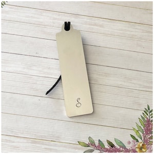 May include: A silver bookmark with a black ribbon and the letter "S" engraved on the front.
