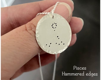 Può includere: Collana con pendente in argento con il design del segno zodiacale dei Pesci. Il pendente rotondo ha una texture martellata e una catena sottile. Il testo "Pisces Hammered edges" è visibile.