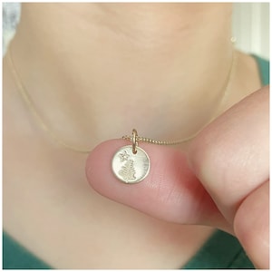 May include: A gold necklace with a small round pendant featuring a tree and a star design.