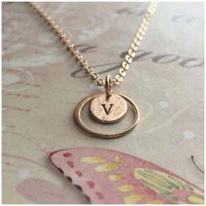 Peut inclure: Un collier en or avec une chaîne délicate et un pendentif composé d'un cercle martelé avec la lettre "V" gravée dessus. Le cercle est entouré d'un cercle ouvert plus grand.