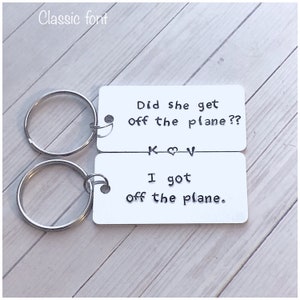 May include: Two silver keychains with a white rectangular tag. The top tag reads "Did she get off the plane??" with the initials "K ♥ V" below. The bottom tag reads "I got off the plane."